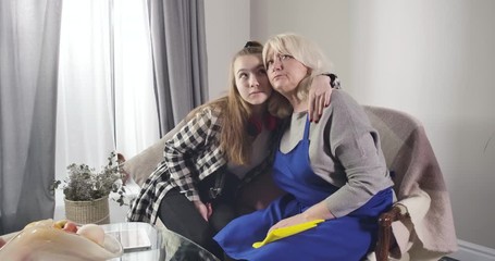 Mature Caucasian woman hugging young granddaughter and looking away. Relatives sitting on couch together and sharing their problems. Good relationship, trust, support. Cinema 4k ProRes HQ.