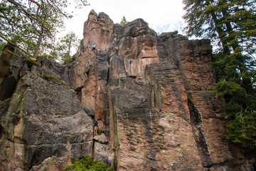 Rock climbers on red cliffband in forested landscape