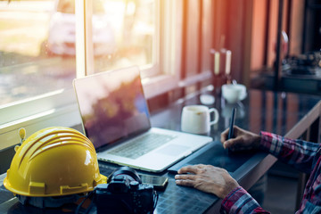 The hands of the engineer are working with the laptop, the yellow helmet, the engineer with the modern office equipment, the construction of the concept