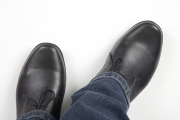 Men's legs in jeans and black classic shoes on white background