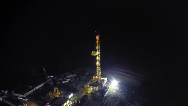 Cinematic night-time drone footage circling the substructure and mast of an onshore oil rig after arriving base camp.