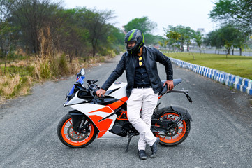 Fototapeta premium Trained biker in black jacket proudly standing near his brand-new sports bike in middle of the road