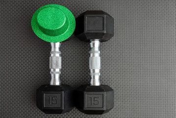 Pair of 15-pound dumbbells on a black gym floor, green leprechaun hat