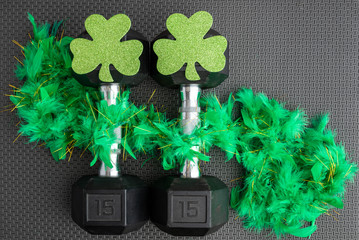 Pair of 15-pound dumbbells on a black gym floor, green feather boa, green shamrocks