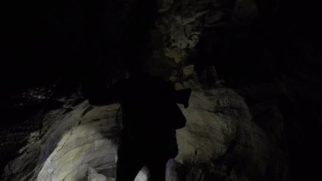 Man exploring small dark cave with flashlight in search of something.