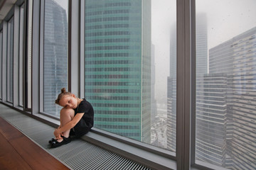 a little girl sits alone at the window of a skyscraper