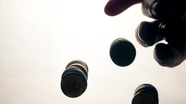 View from below as the hand throws gold coins. Moves them, collects them in the shape of a heart or columns.White background. Indoors.