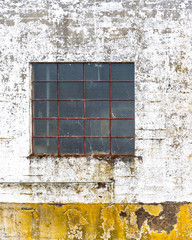 Window with rusty bars on the peeling wall of an old industrial building