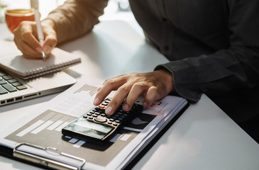 Businessman use the calculator and take notes with calculations about the expenses at the office.