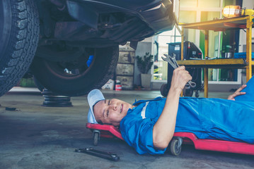Mechanic in blue uniform lying down and working under car at auto service garage.Service and maintenance vehicle concept 