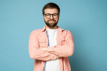 Funny bearded man with glasses stands with arms crossed, smiles strangely and looks at the camera...