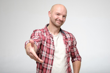 Sweet, good-natured man gives hand for handshake, looking amiably at the camera.