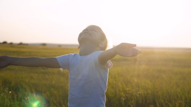 small child hands drawn to heaven concept happy family religion. little boy closed his eyes lifestyle spread his arms to the sides on the nature in the park at sunset slow motion video