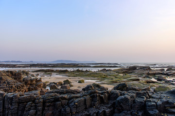Rocky seashore at low tide against the background of the sea and evening sky. Twilight on the coast. In the foreground are large wet stones.