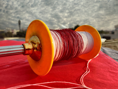 Photograph of a colourful reel of thread, charkhi and manjha, on a bright red coloured kite