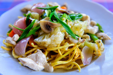 Chinese fried noodles with chicken, vegetables and green onions. Crispy noodles in sauce with cauliflower, mushrooms, chicken fillet, close-up, selective focus.
