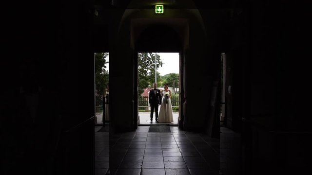Young couple standing at the entrance and ready for wedding ceremony get married, zoom out in the dark aisle