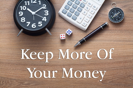 Keep more of your money written on wooden table with clock,dice,calculator pen and compass