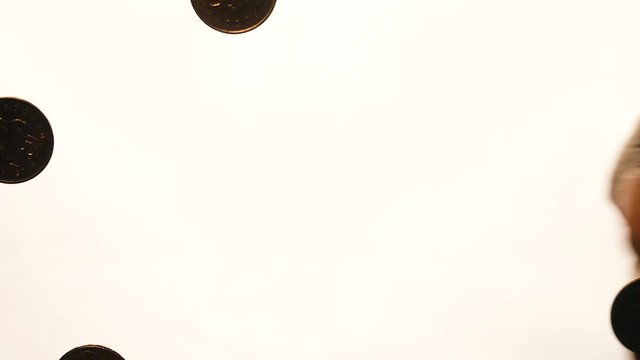 View from below as the hand throws gold coins. Moves them, collects them in the shape of a heart or columns.White background. Indoors.