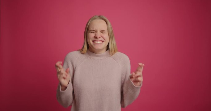 Girl keeping fingers crossed waiting for special moment making wish at pink wall