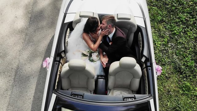 Happy bride kiss groom, newlywed wedding couple is driving a convertible retro car with balloons on a country road for honeymoon after the ceremony. Way. The best day and marriage. Just married.