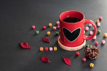 Happy Valentine's Day. Red sweet heart coffee cup, colorful LOVE cube boxes, pieces of flower, pine cone on black background