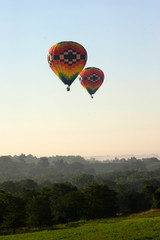 Naklejka premium A pair of hot air balloons slide low over a wooded area during a flight in Iowa.