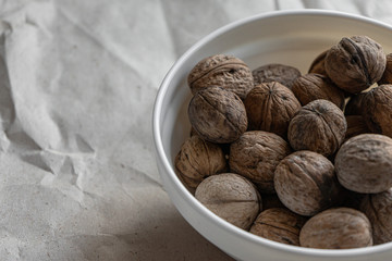 A white plate full of inshell walnuts stands on a brown background from crumpled old kraft paper. Top view flatlay