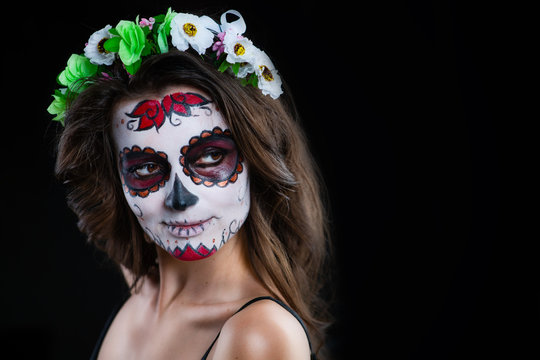 Portrait of a young woman with make-up sugar skull with flowers in her hair on a dark background. Dia de los muertos. Day of The Dead. Halloween costume and make-up.