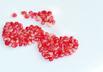 Double heart shaped dark pink pomegranate seeds on a white background.