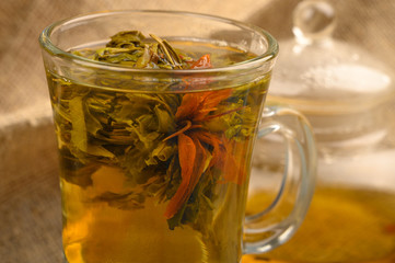 A ball of flower tea brewed in a glass Cup against a background of rough homespun fabric. Close up.