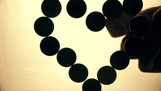 View from below as the hand throws gold coins. Moves them, collects them in the shape of a heart or columns.White background. Indoors.