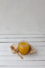 Yellow honey in a glass jar with a wooden spoon. sweet honey on a white wooden background. honey is lying on a white table. space for text. health food. organic food. beekeeper. natural sweets.