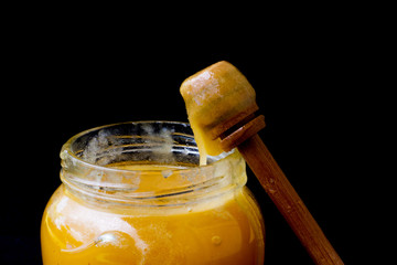 Yellow honey in a glass jar with a wooden spoon. sweet honey on a black wooden background. beekeeper. natural sweets. honey is lying on a dark table. space for text. health food. organic food.