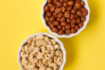 hazelnuts and walnuts in two white cups on a yellow background. lots of nuts. the concept of proper nutrition and health. Healthy food and snacks, organic vegetarian food. the view from the top. 