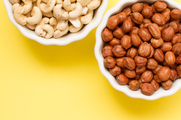 hazelnuts and walnuts in two white cups on a yellow background. lots of nuts. the concept of proper nutrition and health. Healthy food and snacks, organic vegetarian food. the view from the top. 
