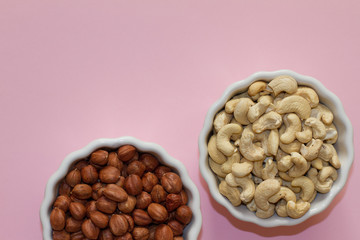hazelnuts and walnuts in two white cups on a pink background. lots of nuts. the concept of proper nutrition and health. Healthy food and snacks, organic vegetarian food. the view from the top.