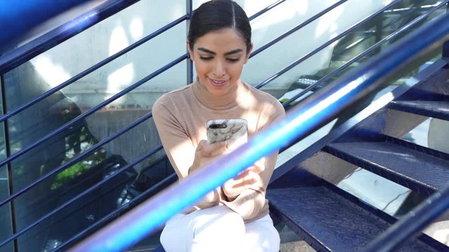 Persian woman using smartphone sitting on urban steps