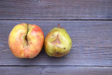 Fresh bio apple and pear ugly with defects lie on a wooden table. No ugly food. place for text