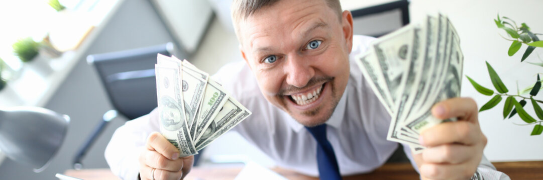 Handsome smiling adult caucasian businessman hold dollar paper cash bancnote in hands against office background. Fast business startup education concept. Financial bill economy project