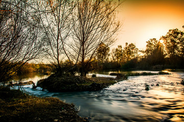 Paisaje rural con el curso del río en movimiento y una mágica puesta de sol con tonos dorados