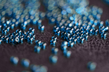 Transparent seed beads blue color scattered on a black leather surface close-up