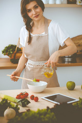 Young brunette woman cooking in kitchen. Housewife holding wooden spoon in her hand. Food and health concept