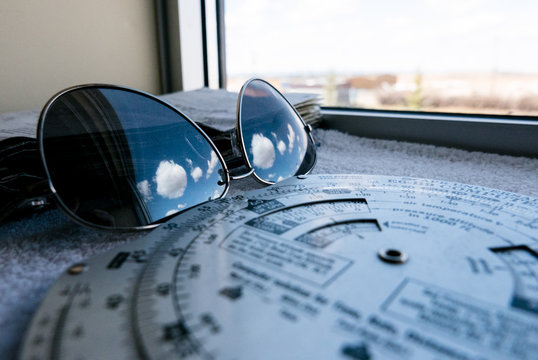 Aviator Sun glasses with blue skies and clouds reflection along with flying tools. Pilot flight prep and tools