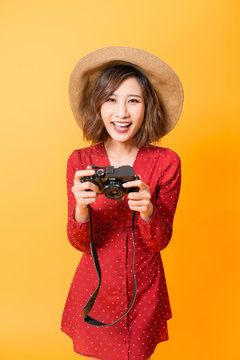 Happy Asian girl looking at her camera while wearing red dress and hat isolated on orange background.
