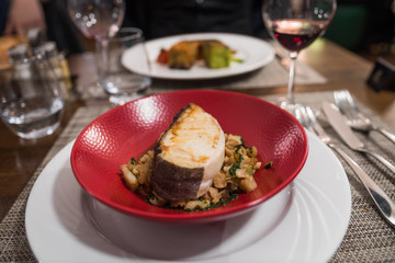 Cooked fish with vegetables served in a red plate. French gastronomic restaurant in Bagnoles-de-l'Orne, Normandy, France. Delicious close up meal.