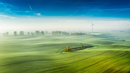 Foggy green field and wind turbine at sunrise