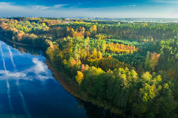 Crystal clear lake with chemtrail reflection and forest, aerial view