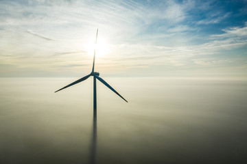 Wind turbine over fog at sunrise with sun rays