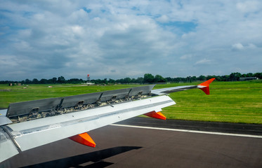 Aircraft wing with extended flaps and spoilers while landing on the runway in the airport - Powered by Adobe